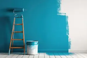 Signs your home’s interior paint needs a refresh shown by a freshly painted blue wall with a paint roller, ladder, and paint can during an interior repaint project