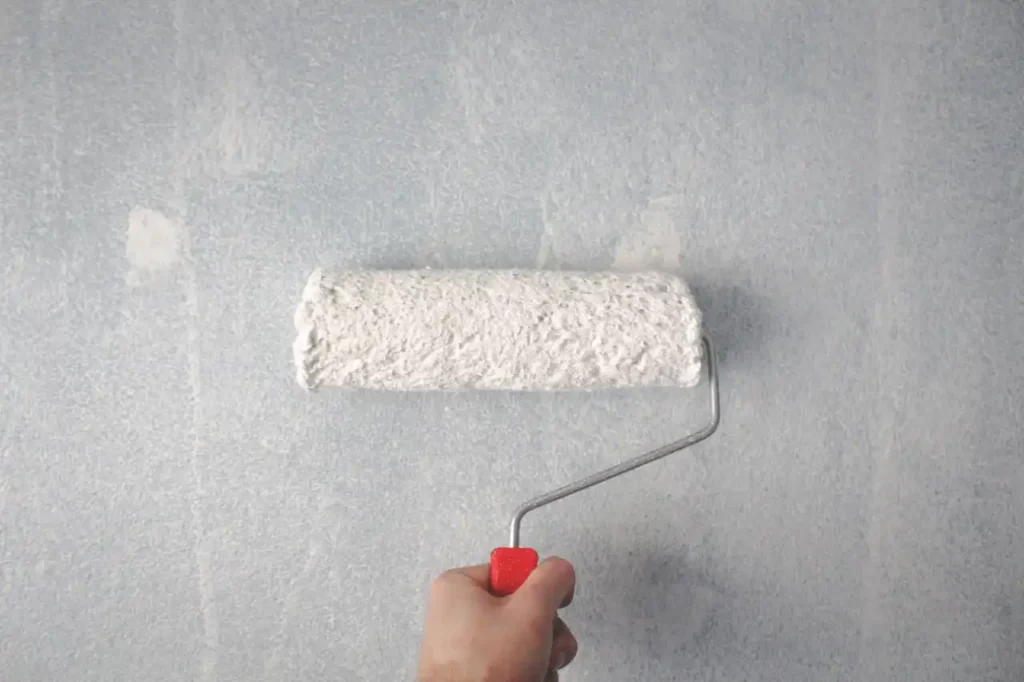hand holding a paint brush with white primer paint painting over dark interior paint on a wall