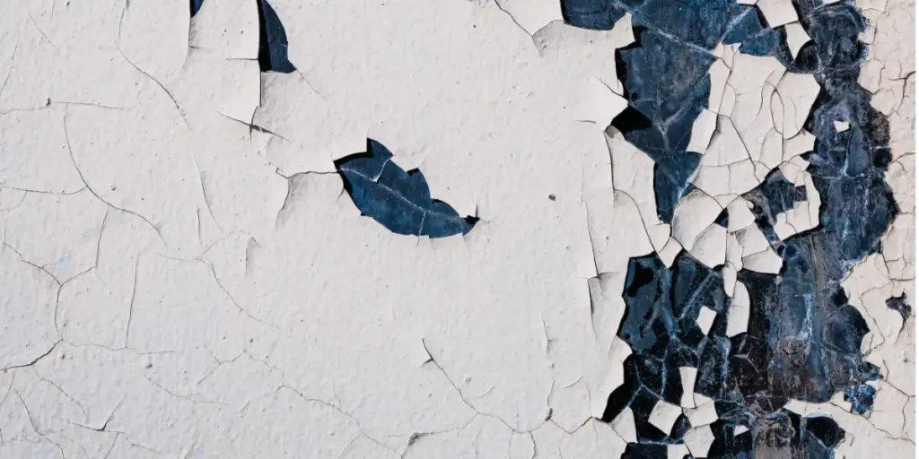 crackling peeling white paint over a dark blue textured paint surface with paint chips