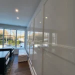 High-gloss white lacquer wall paneling with decorative molding and reflections from large black-framed windows.