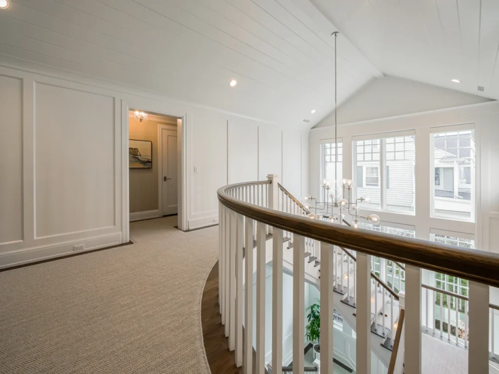 Upper-level hallway overlooking a staircase with neutral walls, white trim, and dark wood railing.