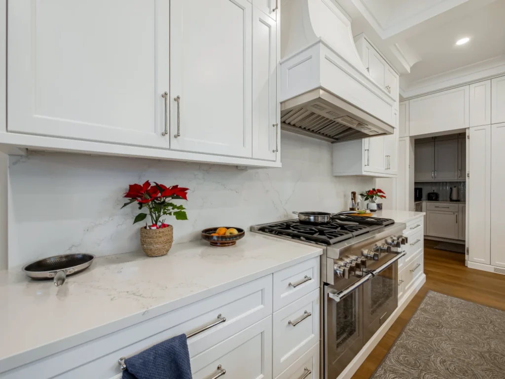 White custom kitchen cabinetry with quartz countertops, a stainless steel range and hood, and warm wood flooring.